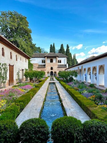 Breathtaking view of Alhambra's Generalife gardens featuring a serene waterway and colorful flowerbeds.