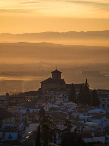 An atmospheric view of Granada, Spain, under a misty sunset sky, showcasing silhouette and urban charm.