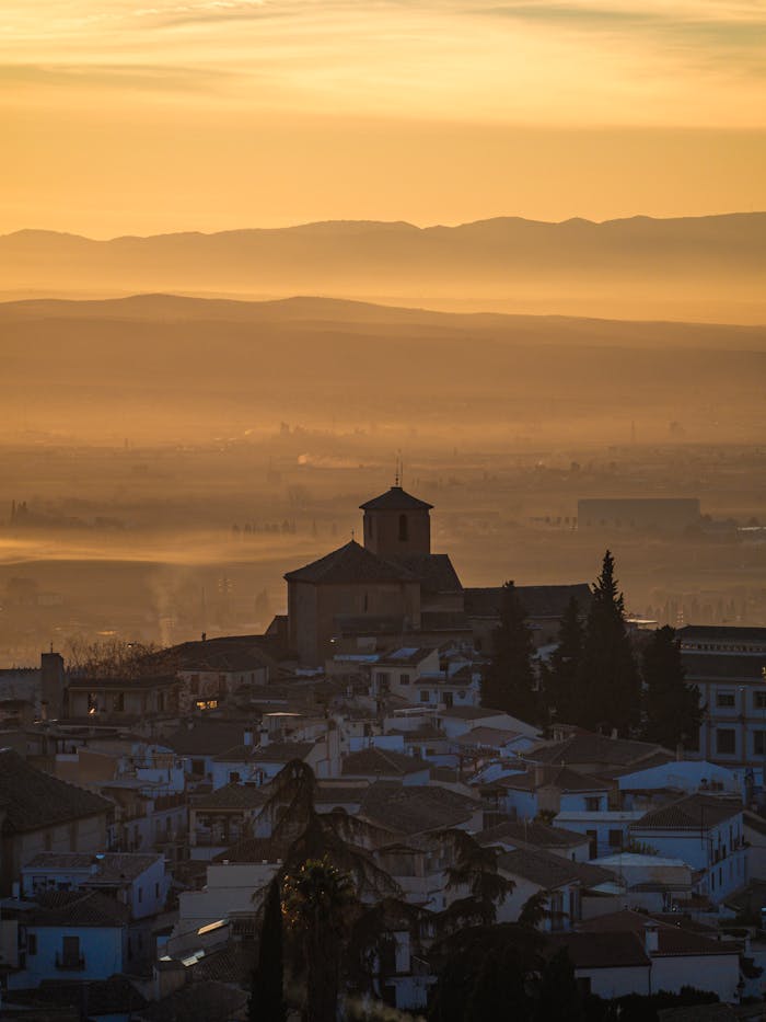 An atmospheric view of Granada, Spain, under a misty sunset sky, showcasing silhouette and urban charm.