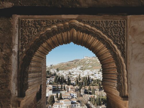 A beautifully ornamented archway in the Alhambra frames a picturesque view of Granada, Spain.