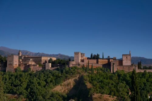 Scenic view of Alhambra Palace, Granada, framed by lush greenery and mountains.